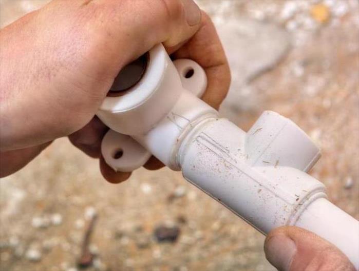 The plumber connects parts of the plastic water pipe using fittings, hands close-up.